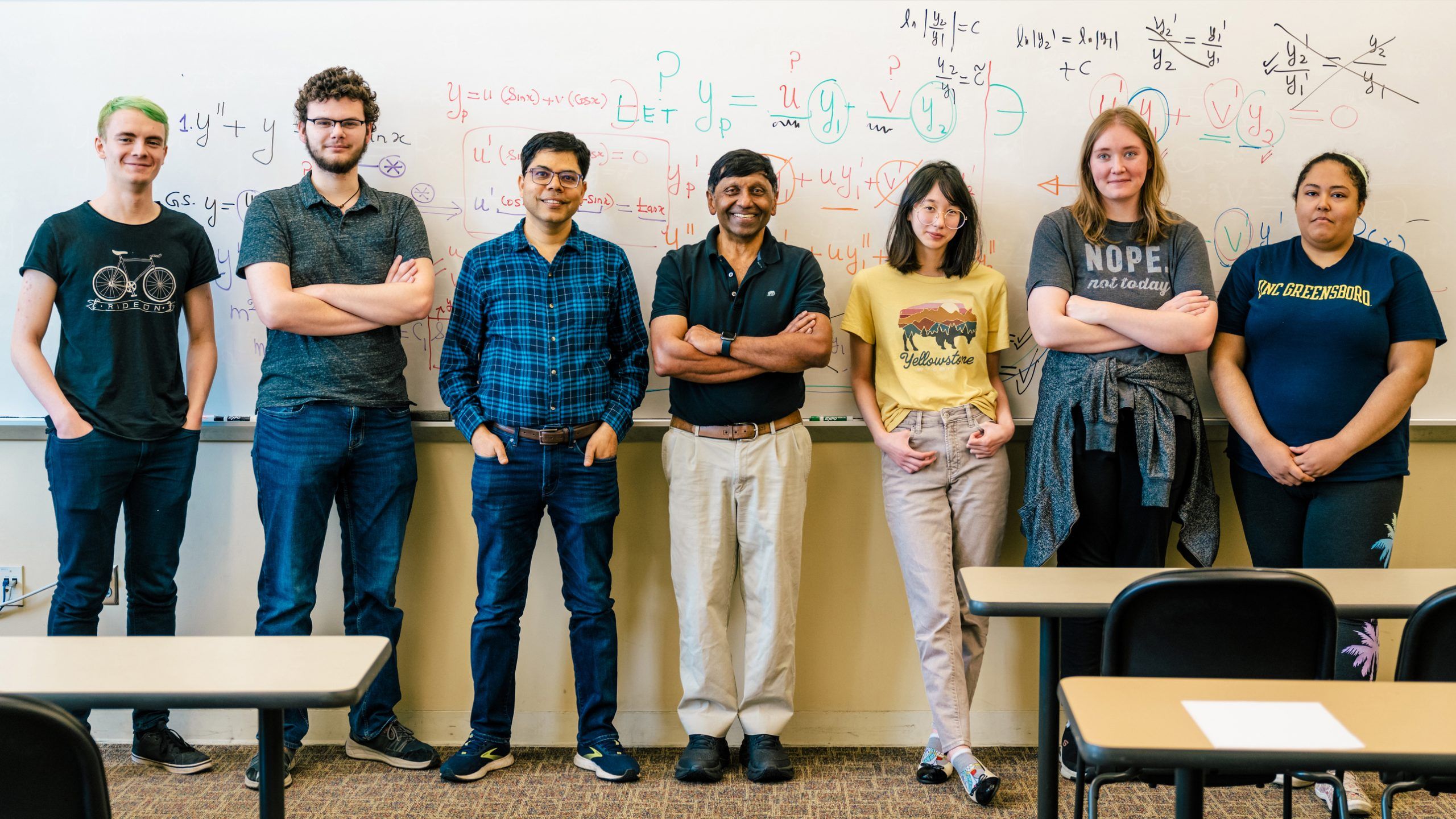 Dr. Shivaji stands with six students in front of a whiteboard covered in math equations, all smiling and posing for a group photo in the classroom.