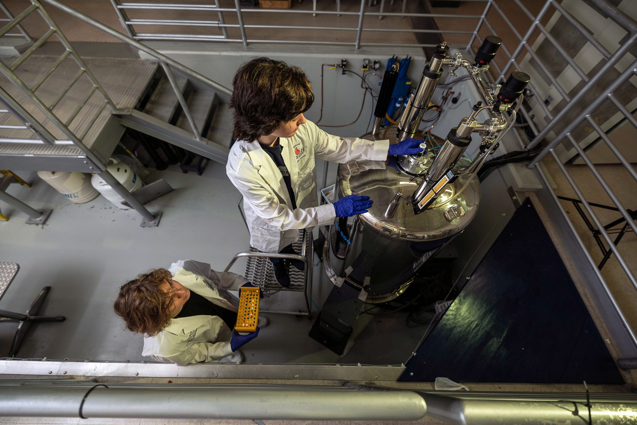 Two students in lab coats working on a nuclear magnetic resonance spectrometer