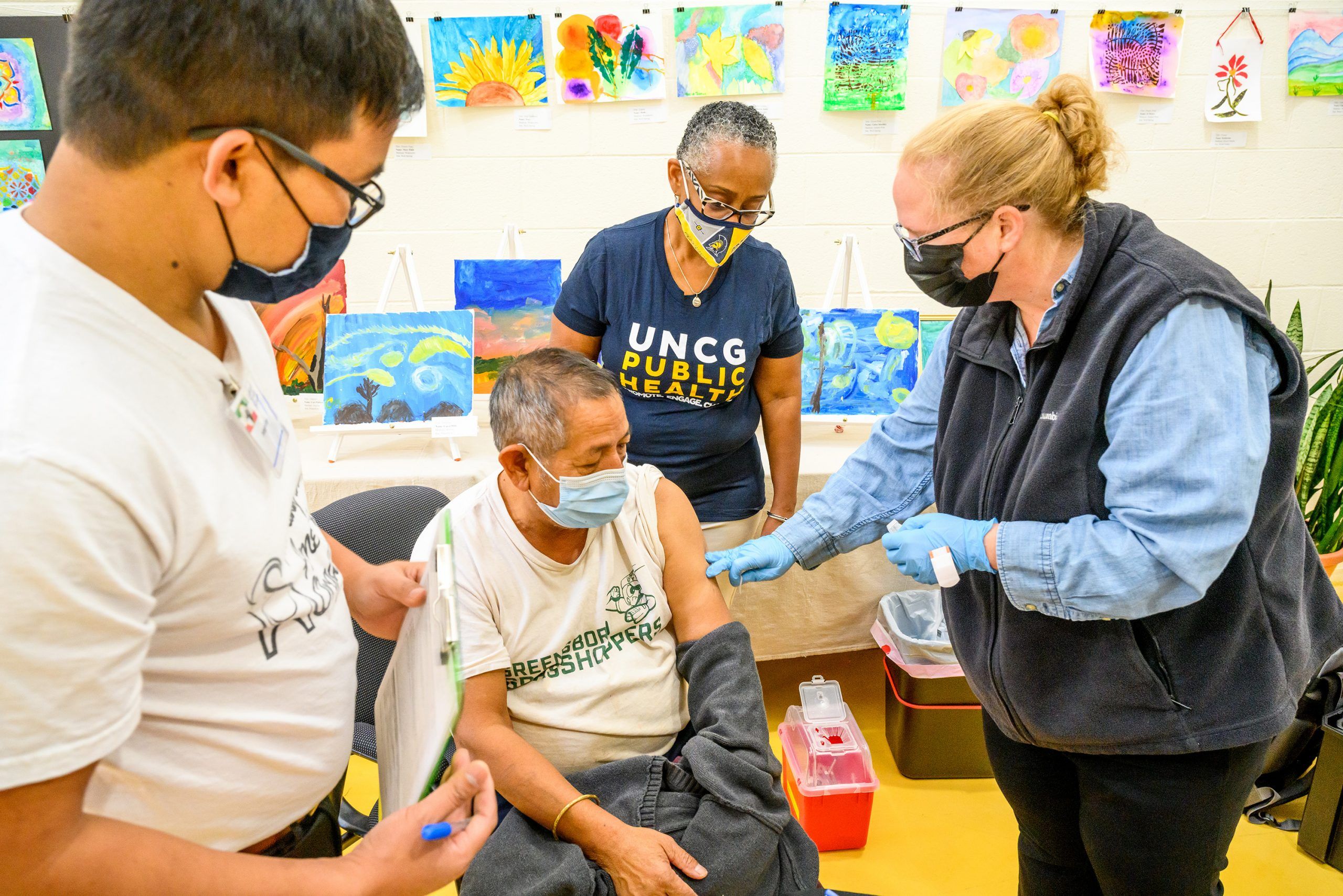 Dr. Morrison and Siu assist at a vaccine clinic, standing by as a man receives a dose of vaccine from a nurse.