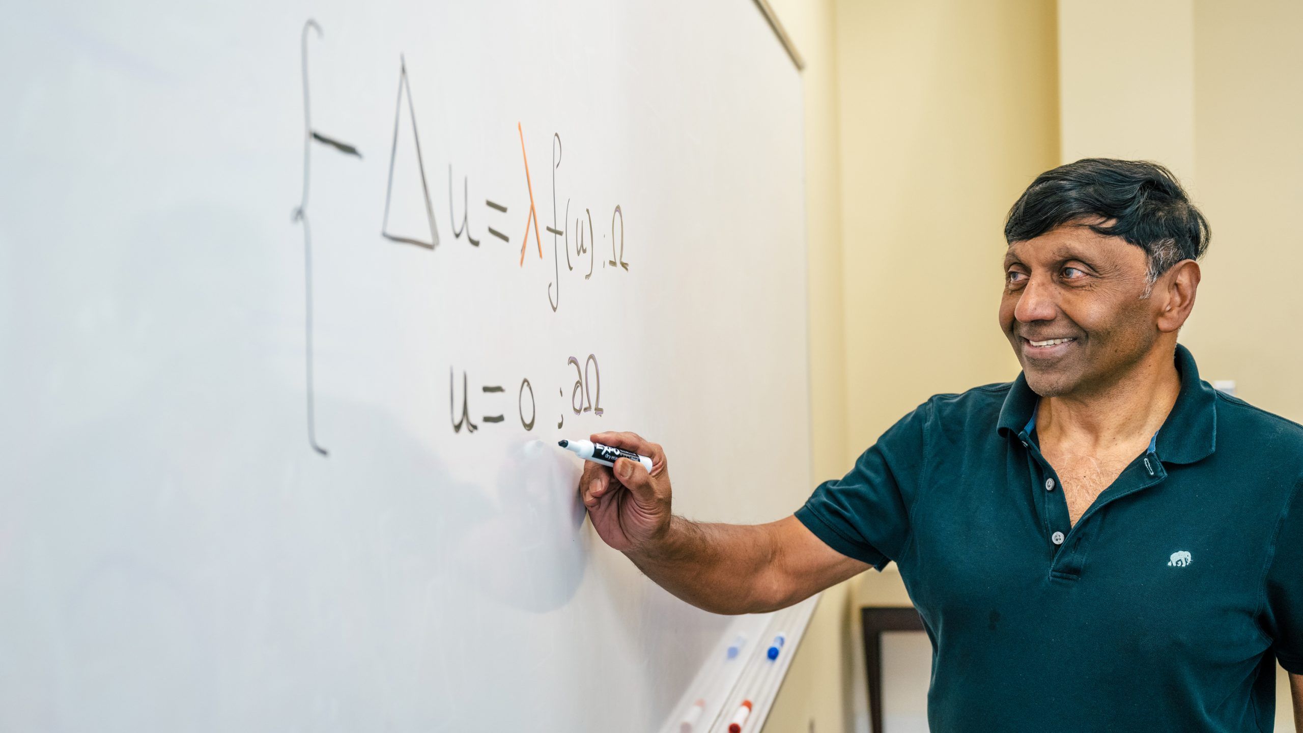 Dr. Shivaji smiles while writing a math equation on a whiteboard during class.