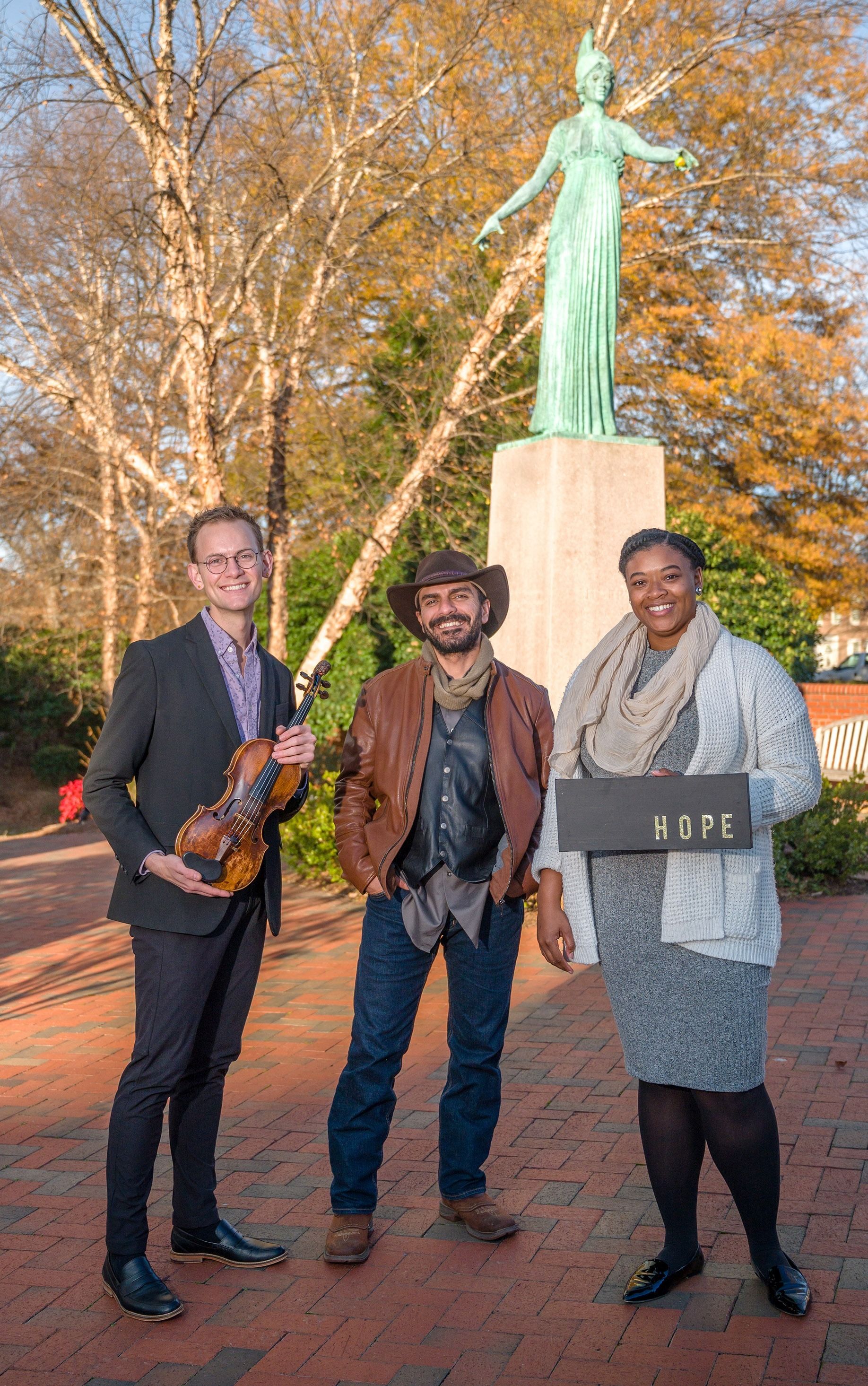 Minerva Graduate Scholars Nathan, Joseph, and Indya stand in front of a statue of Minerva.