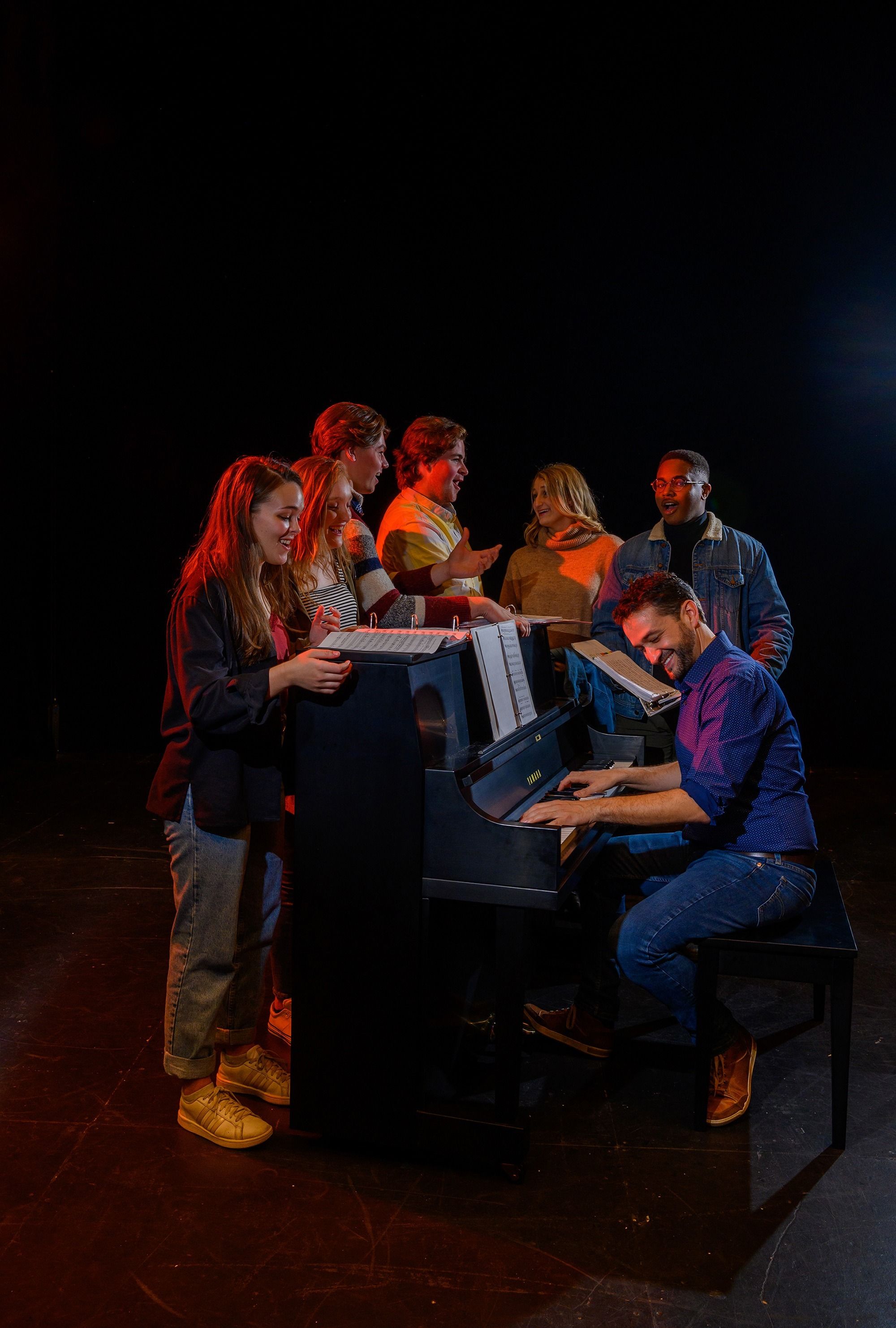 Amendum plays the piano while rehearsing a musical piece with a group of students.