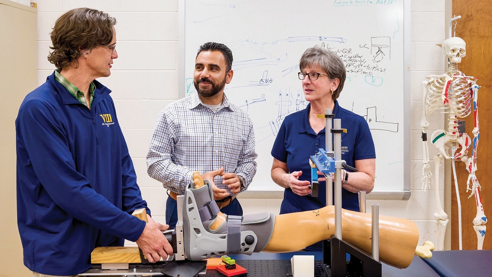 Three researchers discuss a new device using a model of a human leg.
