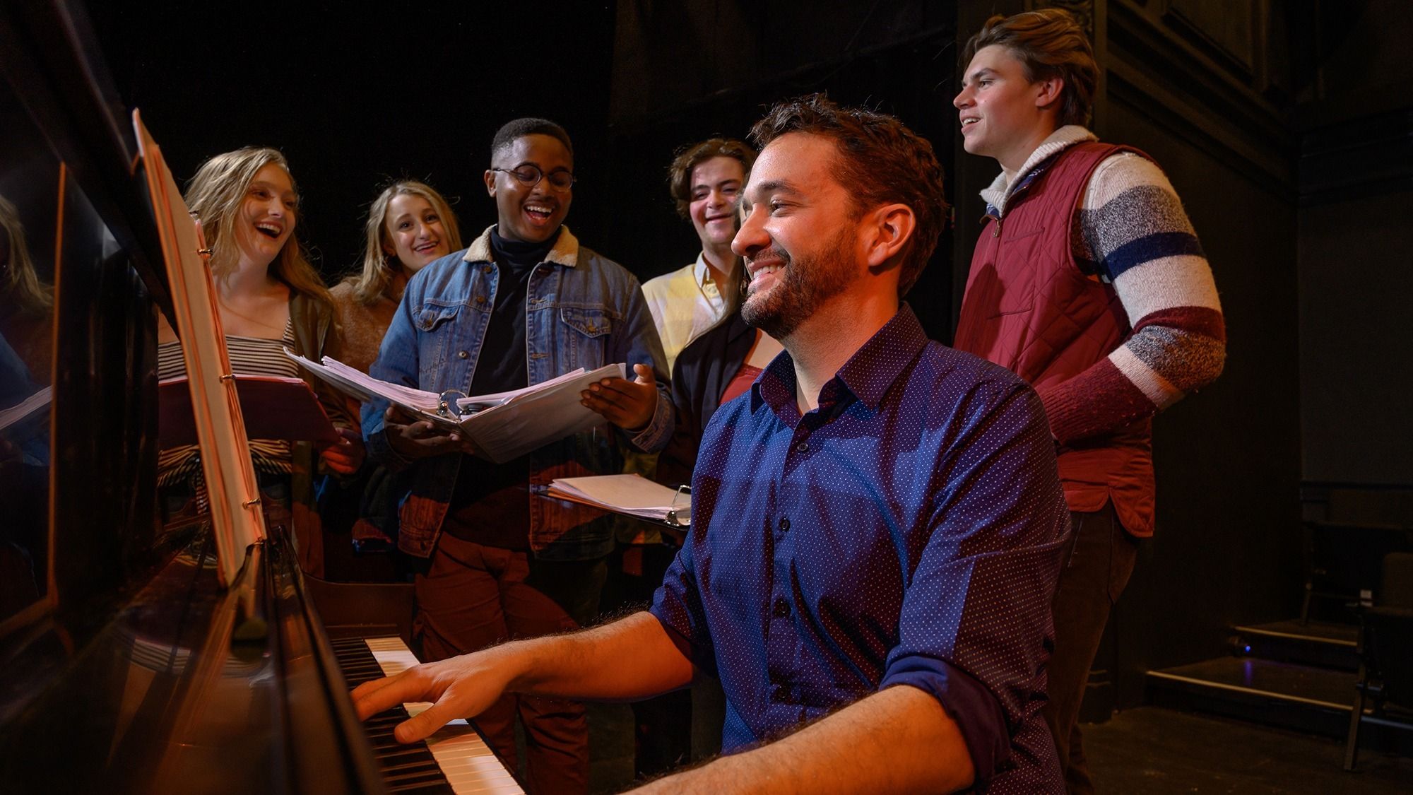 Dominick Amendum at the piano, rehearsing a musical piece with a group of students.
