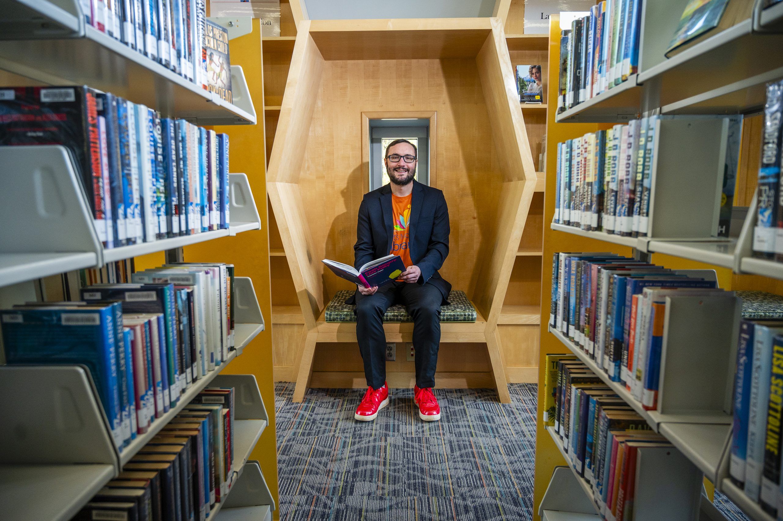 Dr. Noah Lenstra holds a book open in as he sits in a reading nook