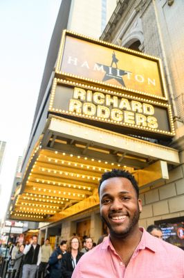Alumnus Deon'te Goodman stands under the sign for Hamilton on Broadway.