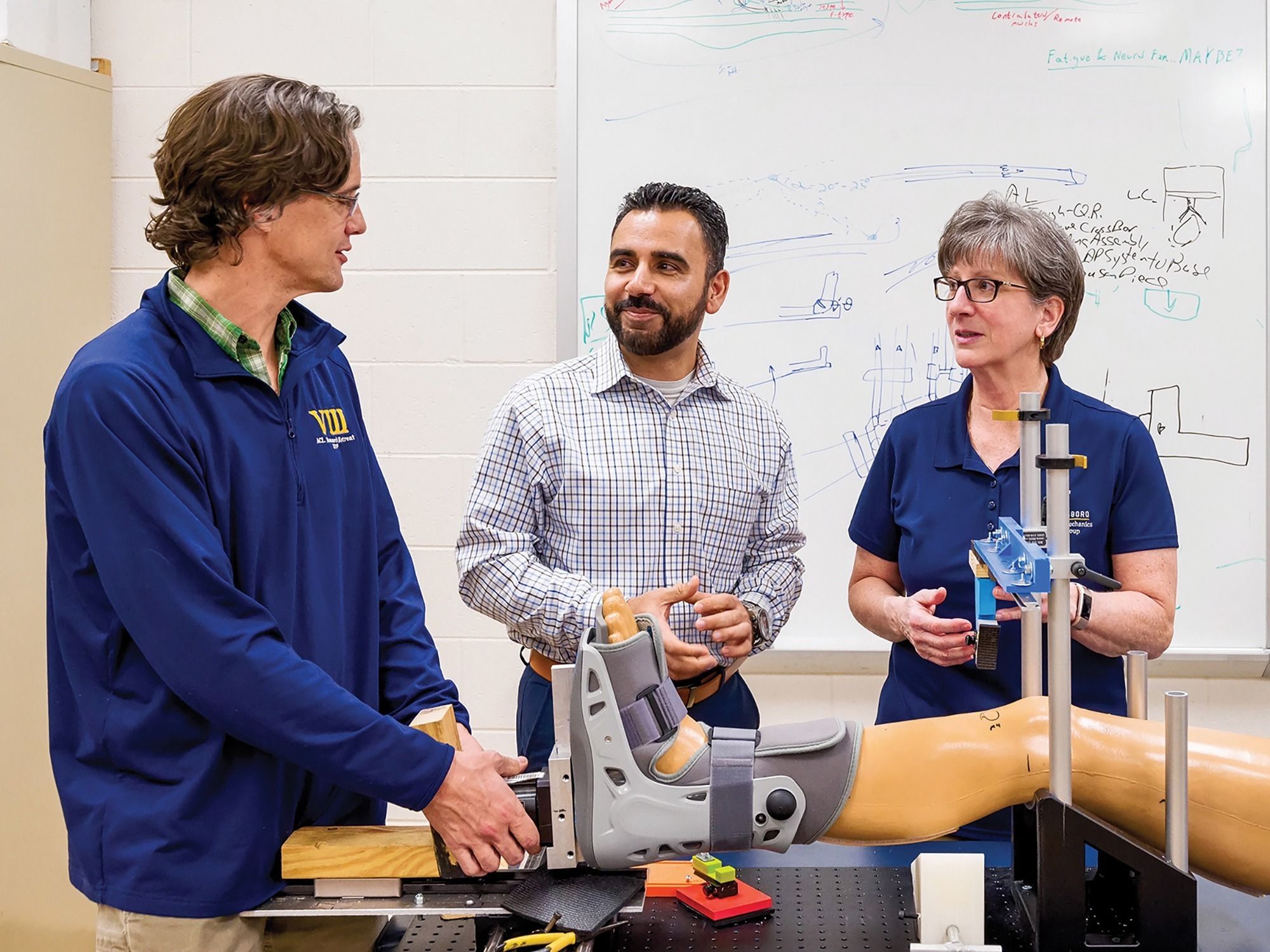 Three researchers use a model of a human leg to discuss a device for measuring knee laxity.