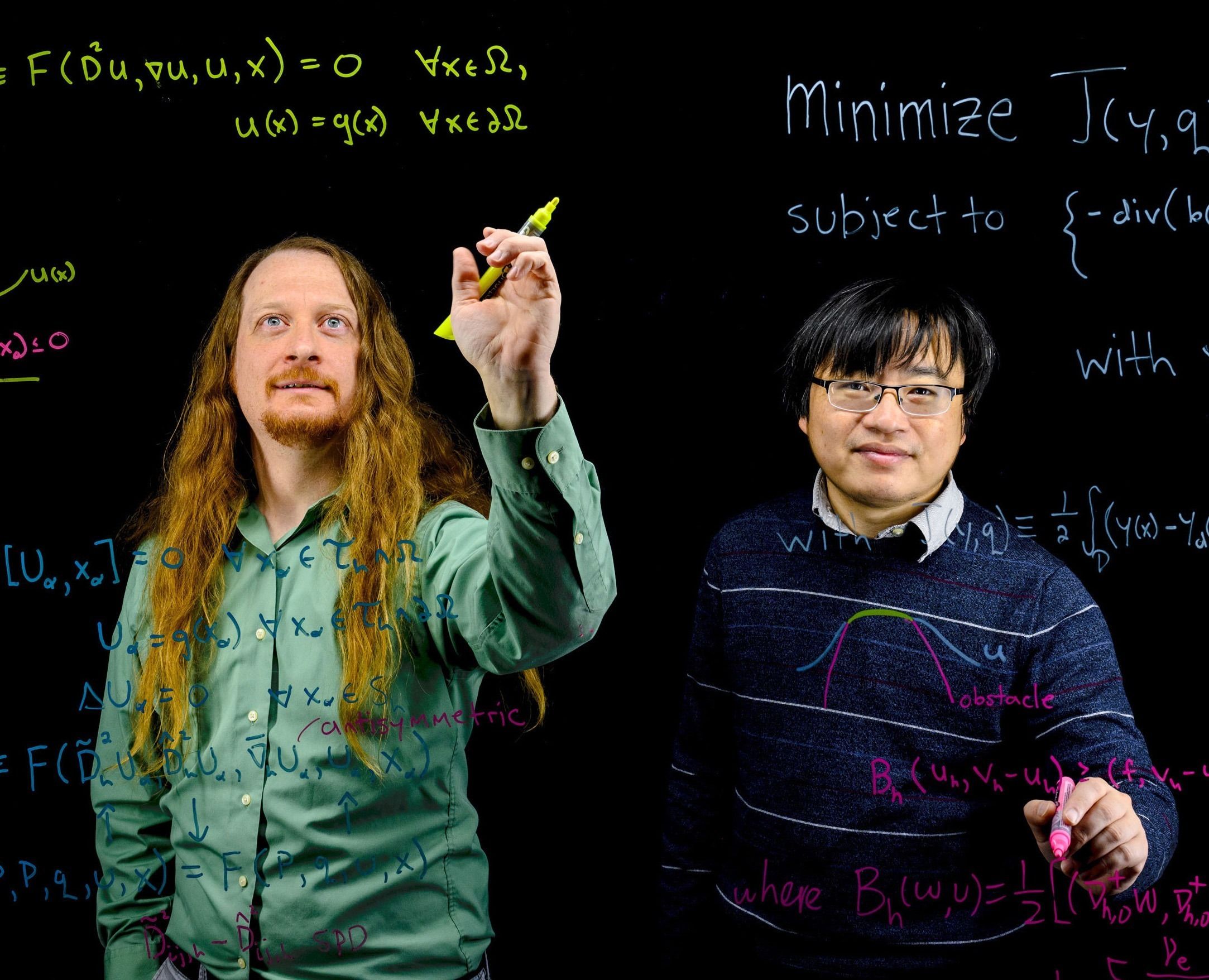 Drs. Tom Lewis and Yi Zhang write differential equations on a transparent whiteboard. 