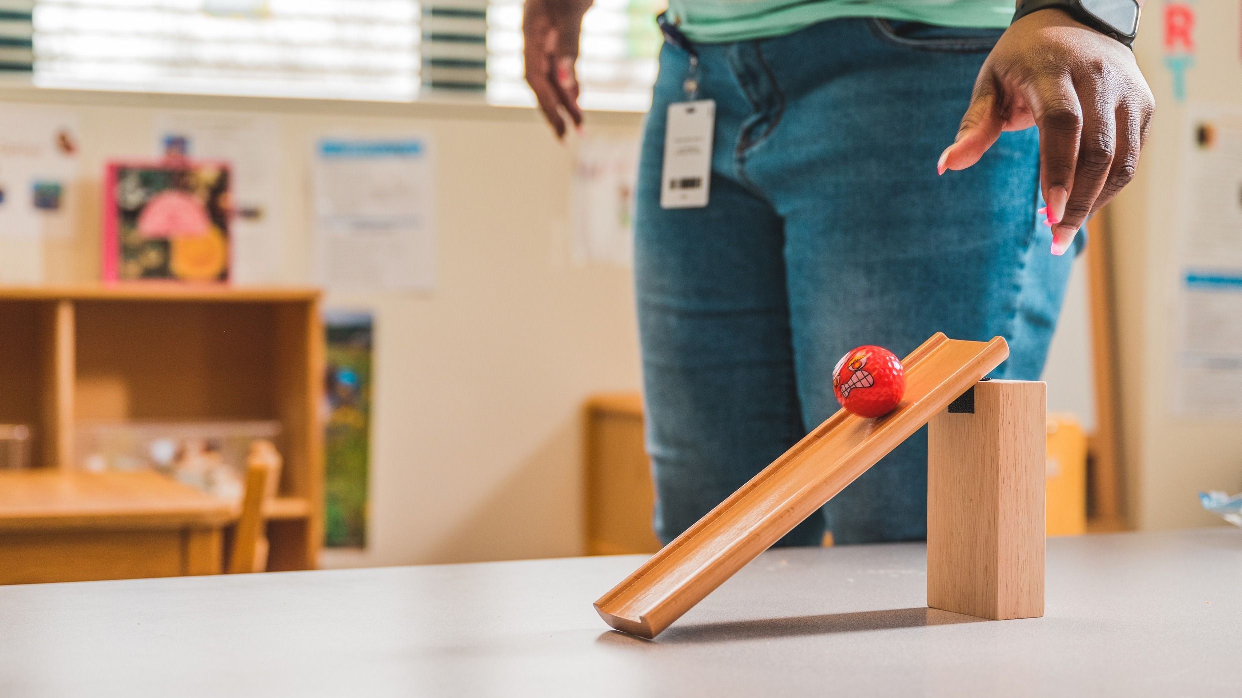 A red golf ball rolling down a wooden ramp.