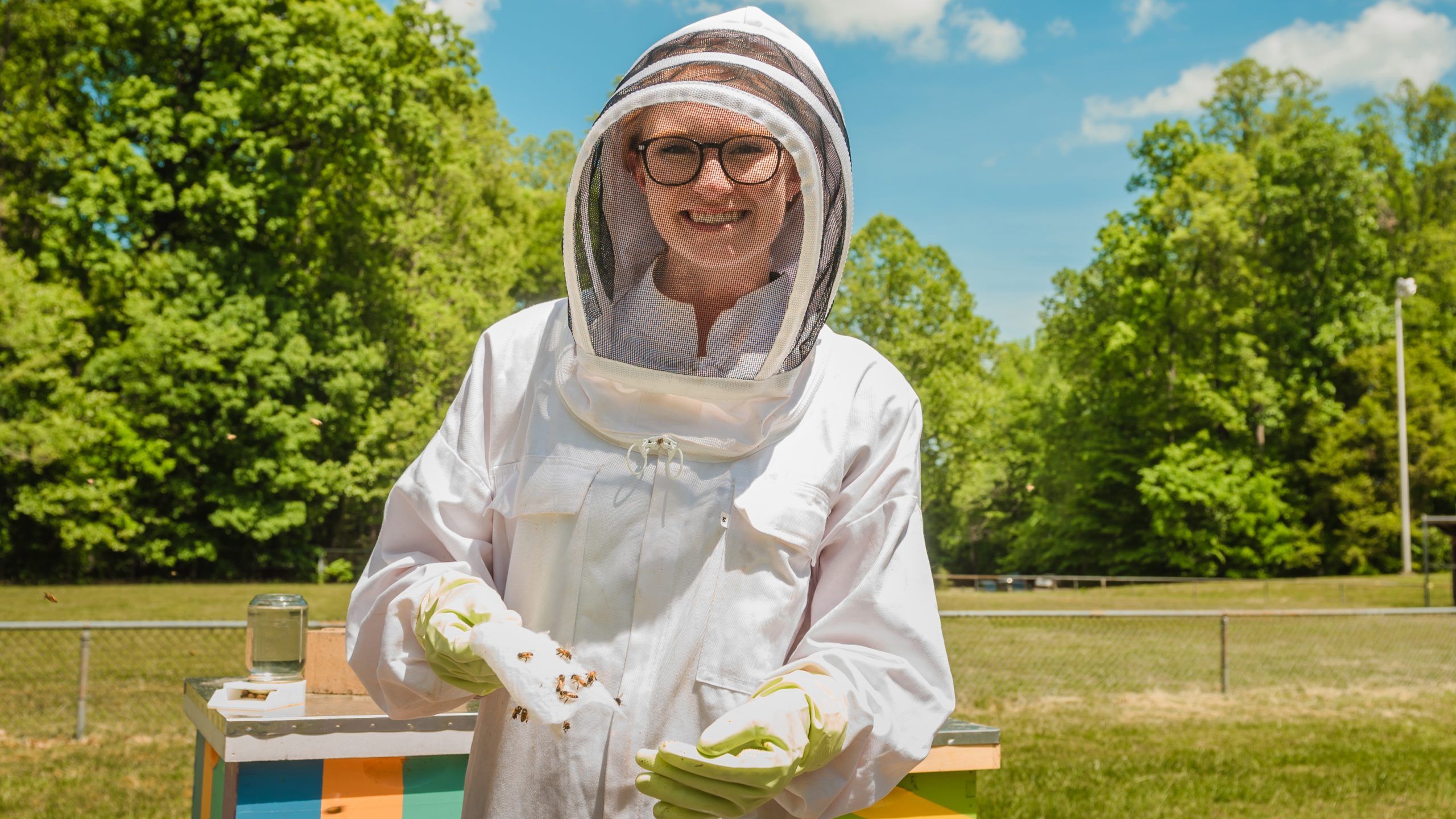 Kasie Raymann in a bee suit holding beekeeping supplies