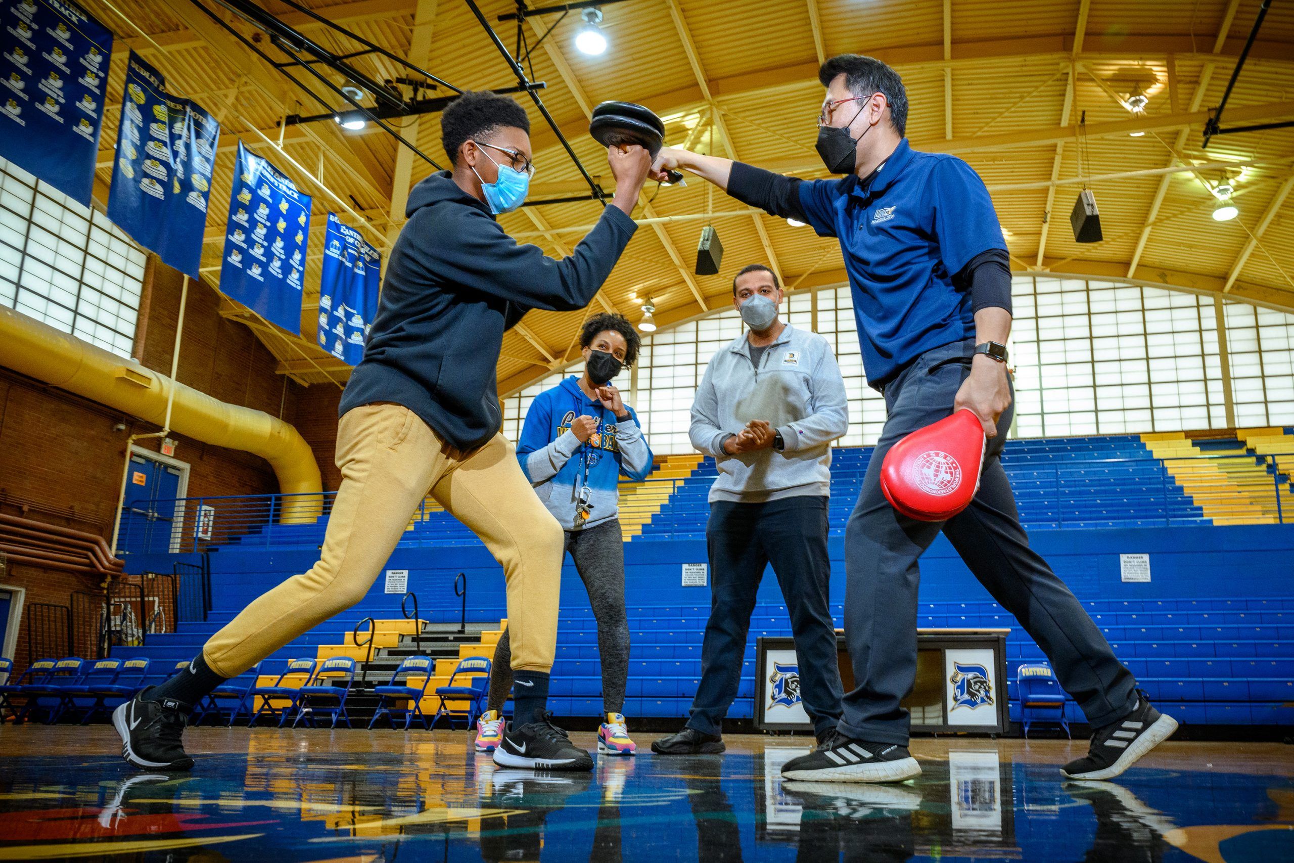 Grad student Yongsun Lee teaches a high school student taekwondo while Dr. Michael Hemphill and the school's coach look on.