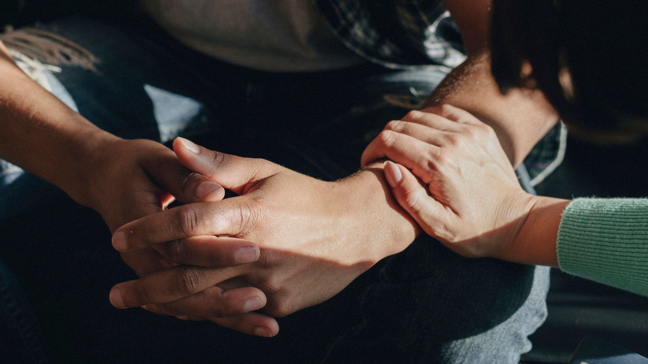 Close-up of one person resting their hands together while another person places a hand gently on their wrist in a gesture of comfort.