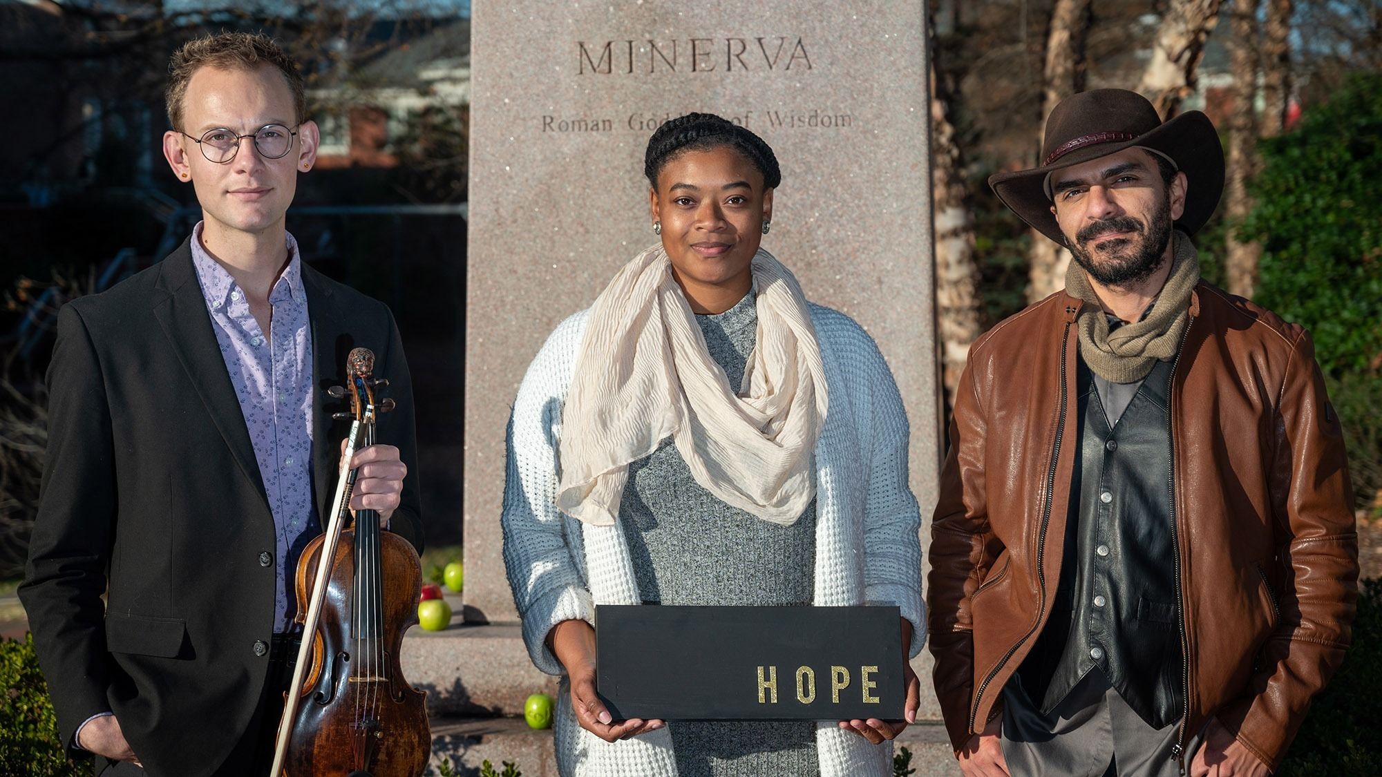 Minerva Graduate Scholars Nathan, Indya, and Joseph stand in front of a statue of Minerva.