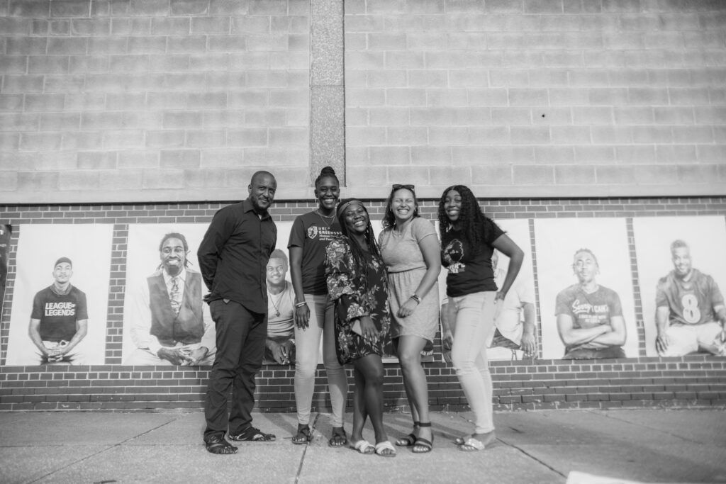 UNCG Grad students standing in front of a mural in Baltimore with photographer Zizwe Allette.