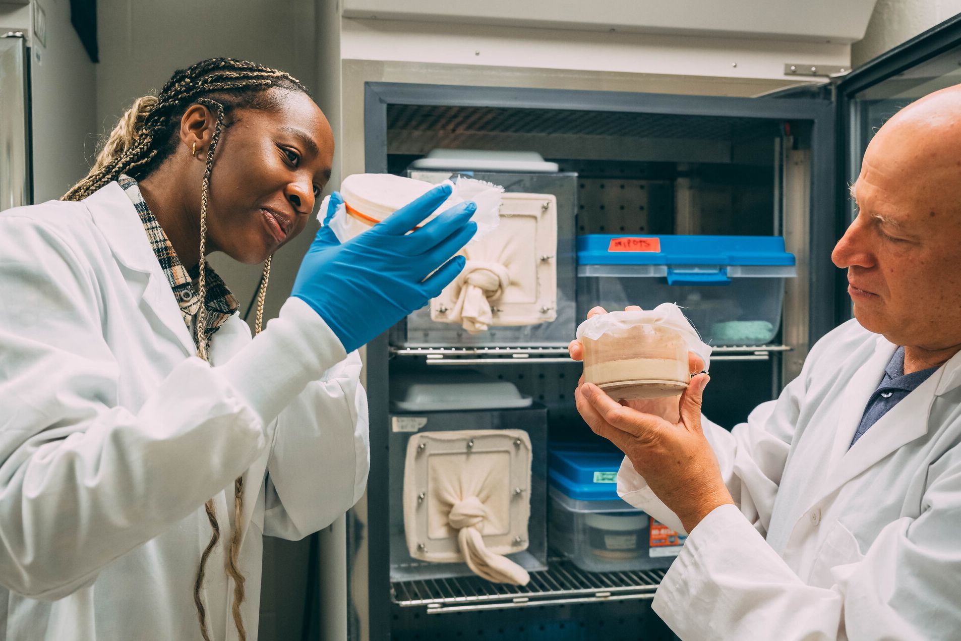 Two people in lab coats, one wearing protective gloves while pointing at a screen.