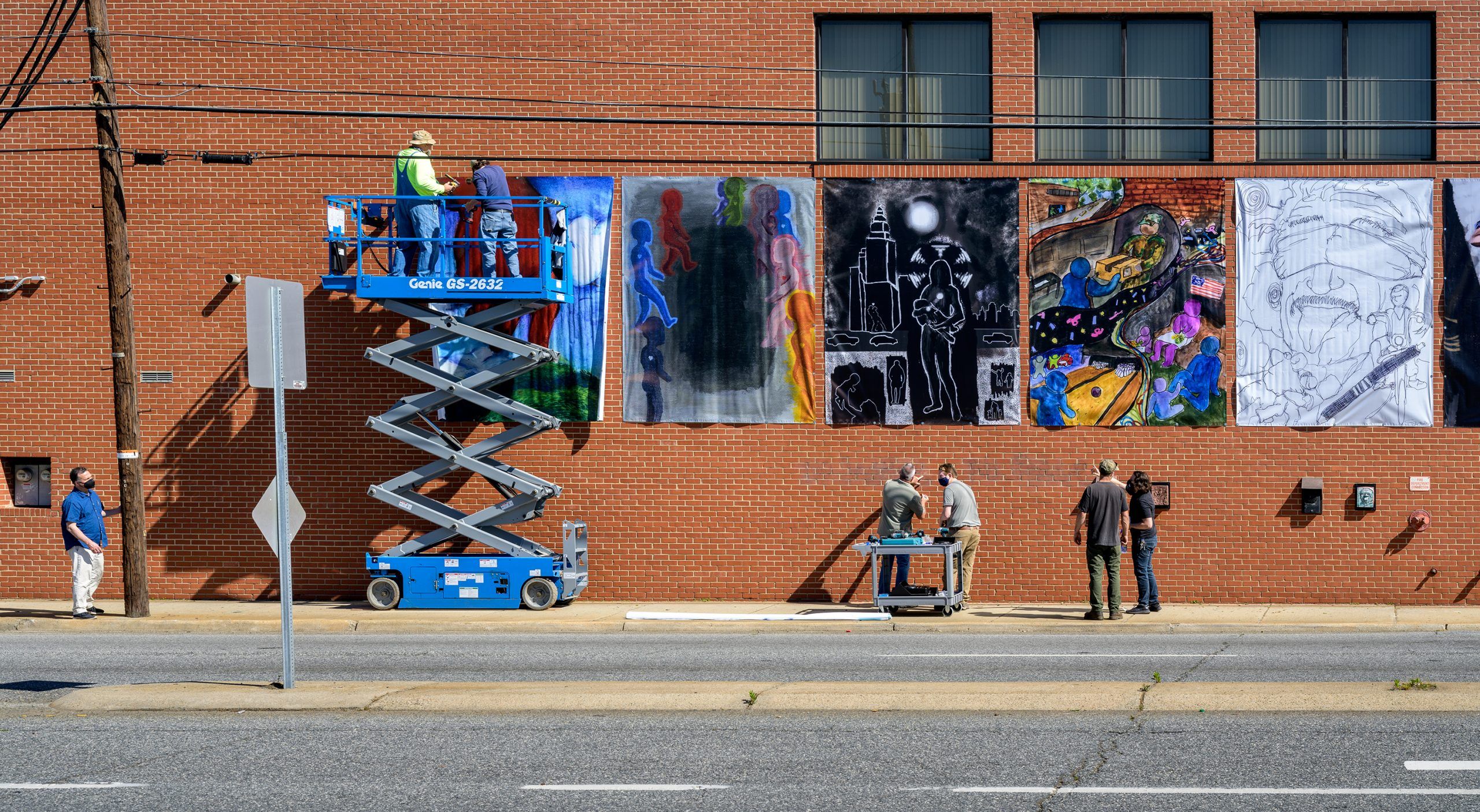 Employees hanging up pieces made by UNCG students