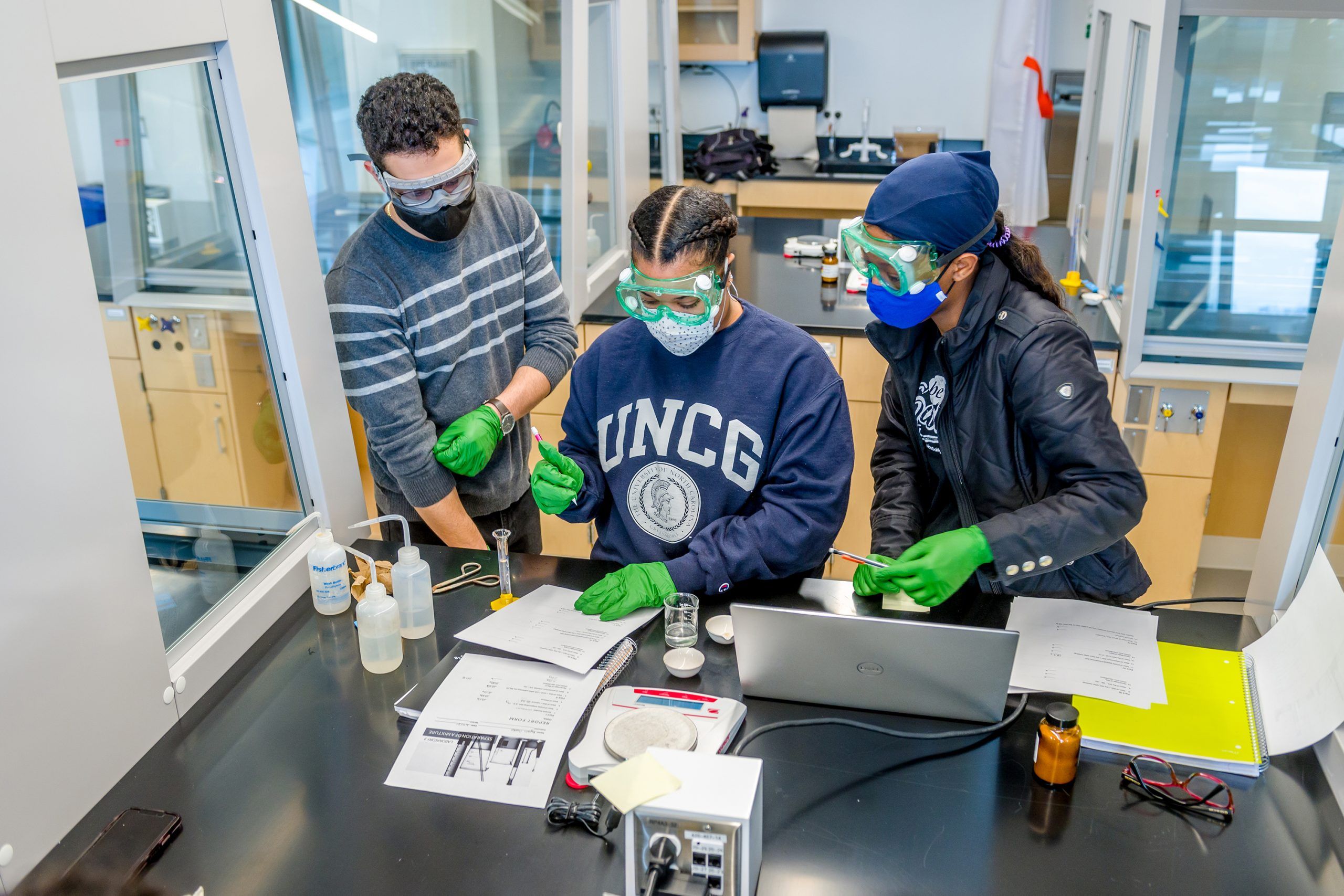 Three students in safety goggles doing lab work.