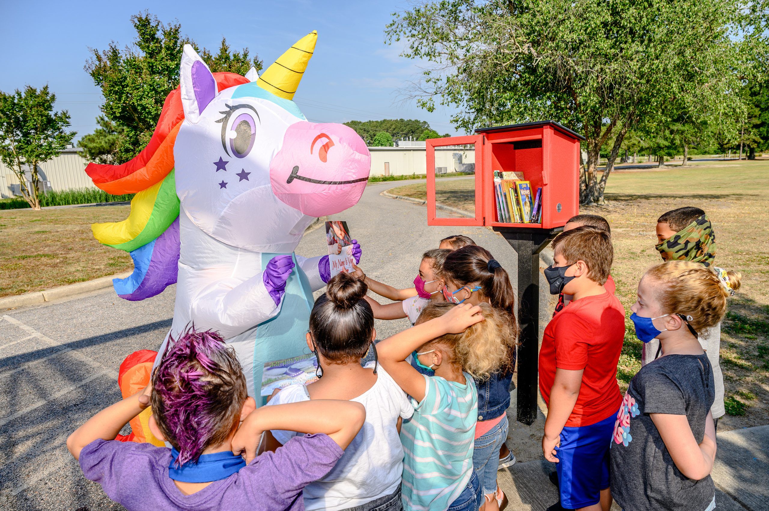 Children looking at a book a unicorn mascot holds