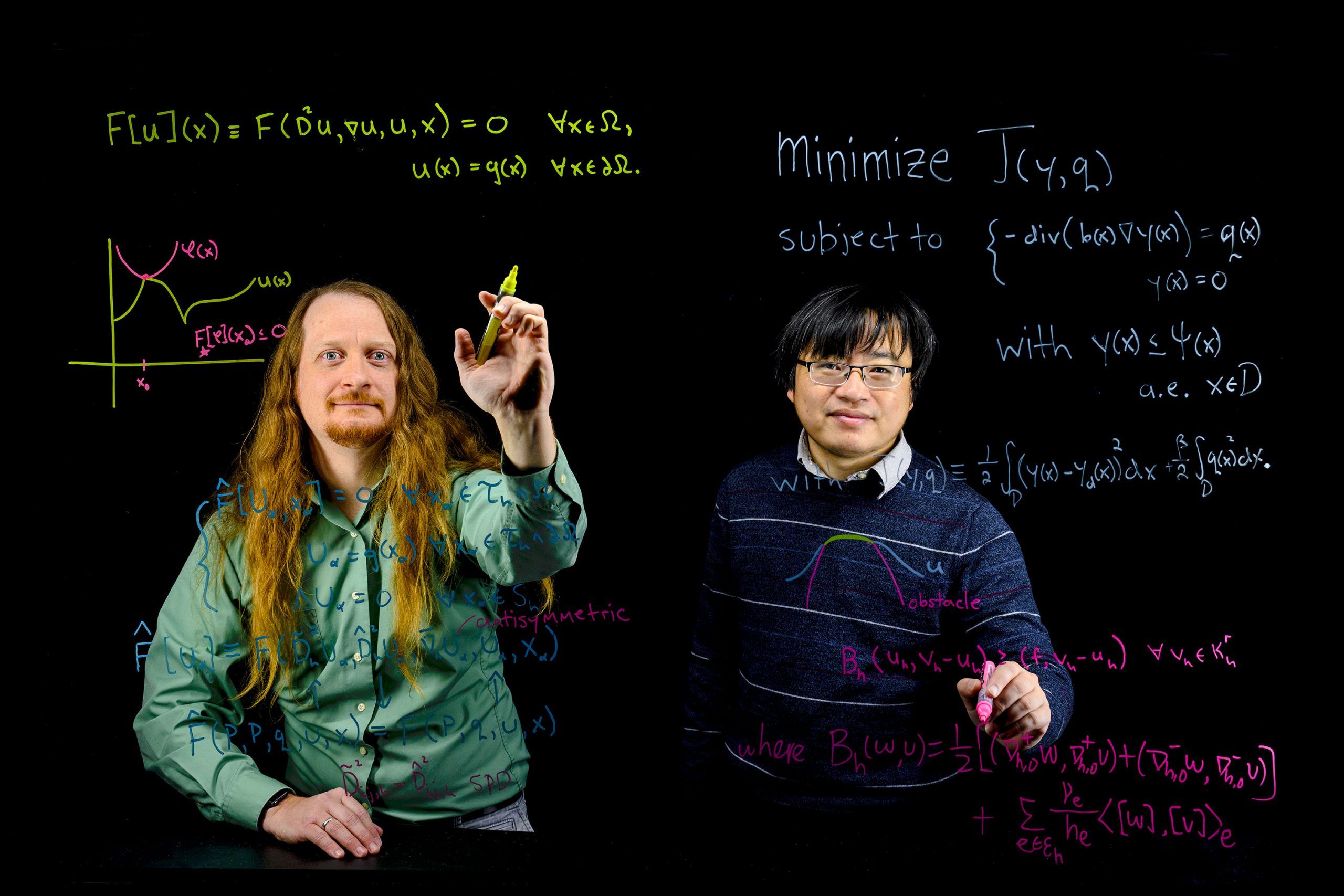 Drs. Tom Lewis and Yi Zhang write equations on a transparent board.