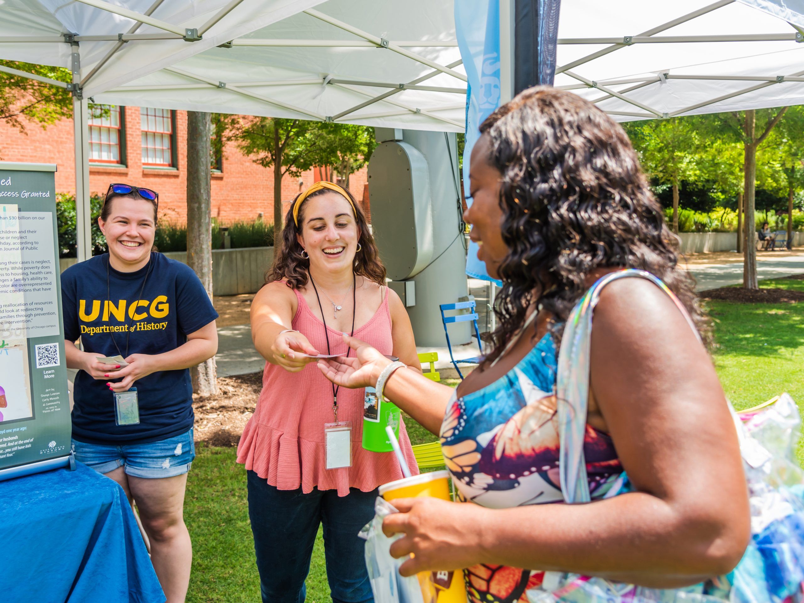 Two UNCG volunteers talk with a woman at a Democracy tables event, and hand her an information card.