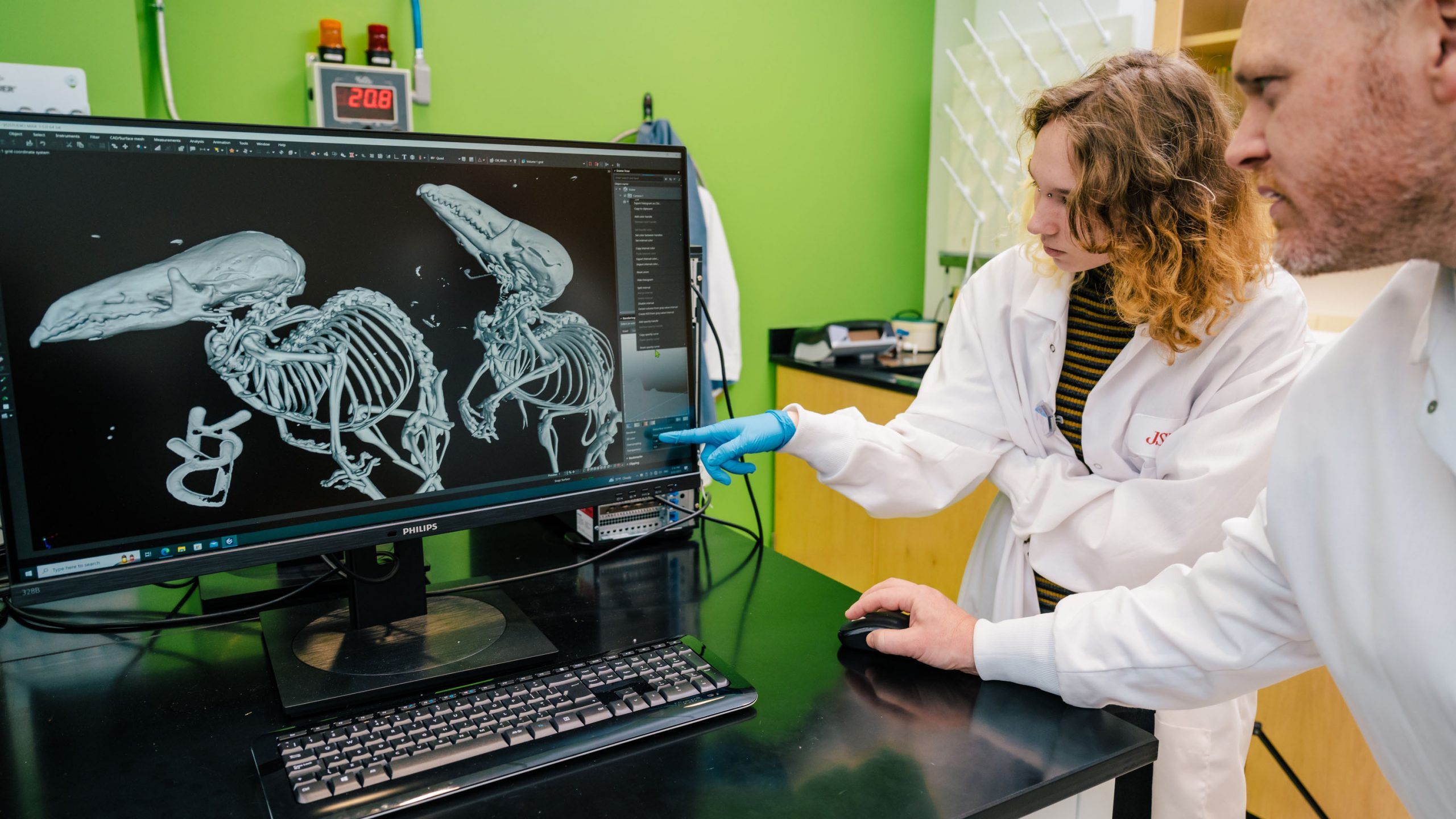 Two people wearing lab coats examining scanned fossils on a computer monitor. 