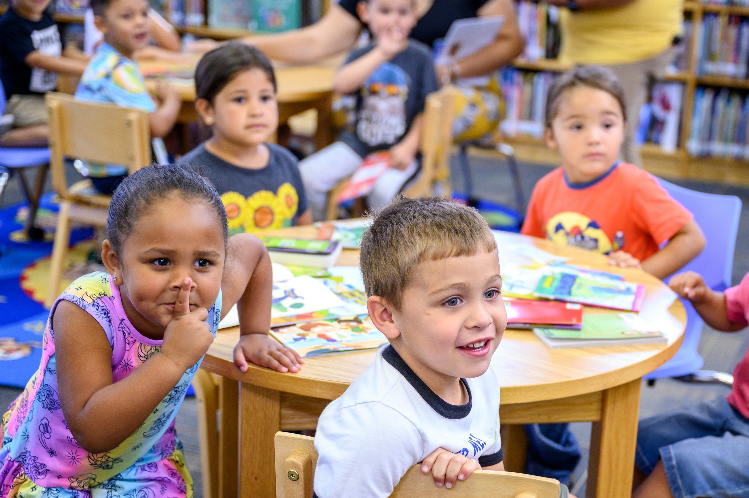 Five children at a table filled with books staring