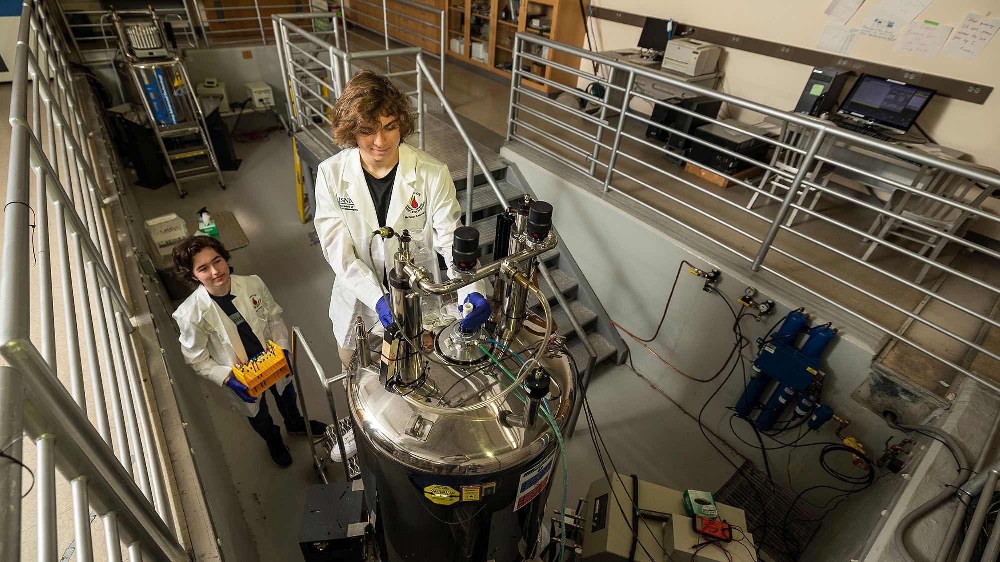 Two students wearing lab coats work on machinery in a lab.