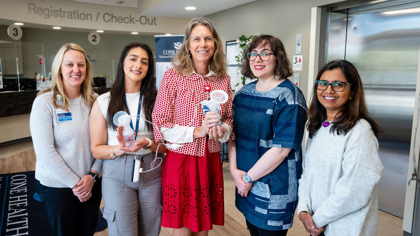 Jigna Dharod, Jasmine DeJesus, grad student Selene Villa, and Cone Health's Marjorie Jenkins and Julie Wenzel stand in the lobby and hold breast pumps