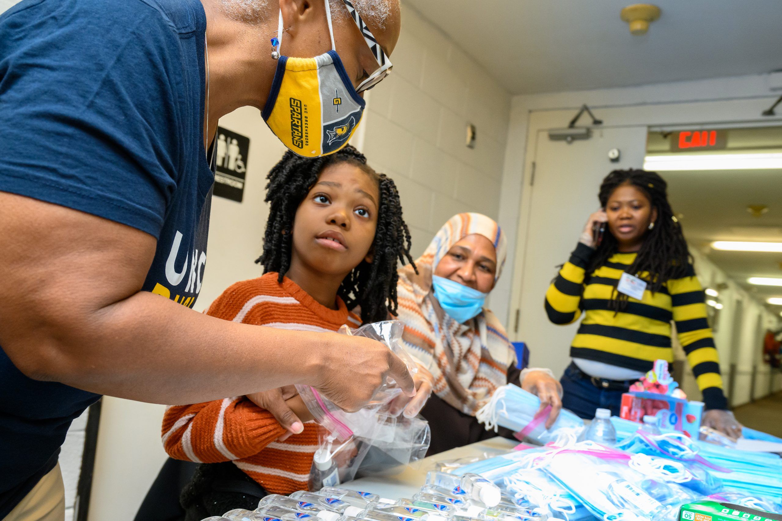 Dr. Morrison and community partners Siddiga Ahmed and Satta Sedi, and Sedi's daughter, sit at a table assembling PPE bags.