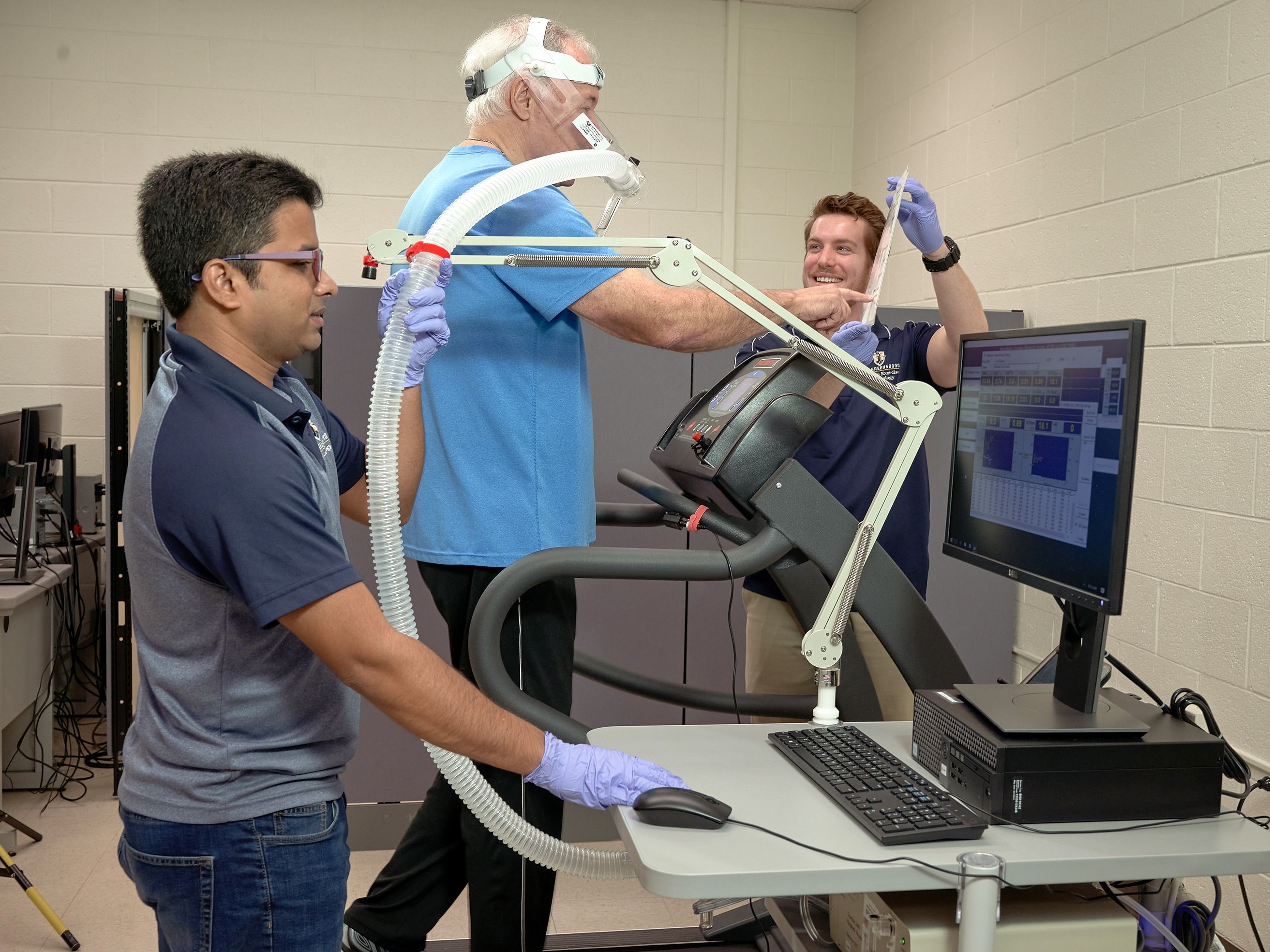 Two grad students evaluate a participant's fitness by measuring respiration and perceived exertion on a treadmill.