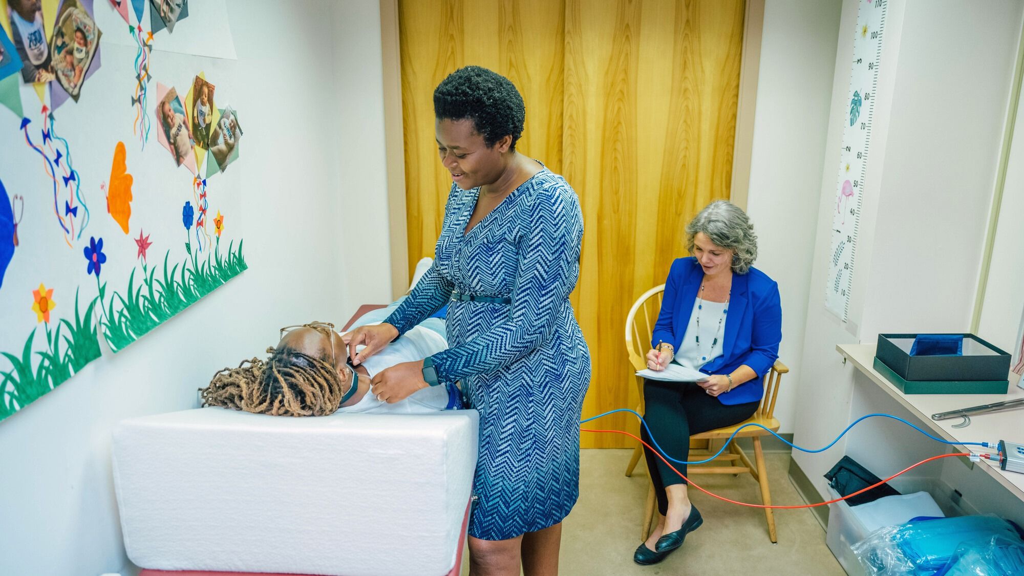 Dr. Forgive Avorgbedor demonstrating the use of a Vicorder, a device to assess arterial stiffness on PhD student Favour Omondi while Esther Leerkes observes