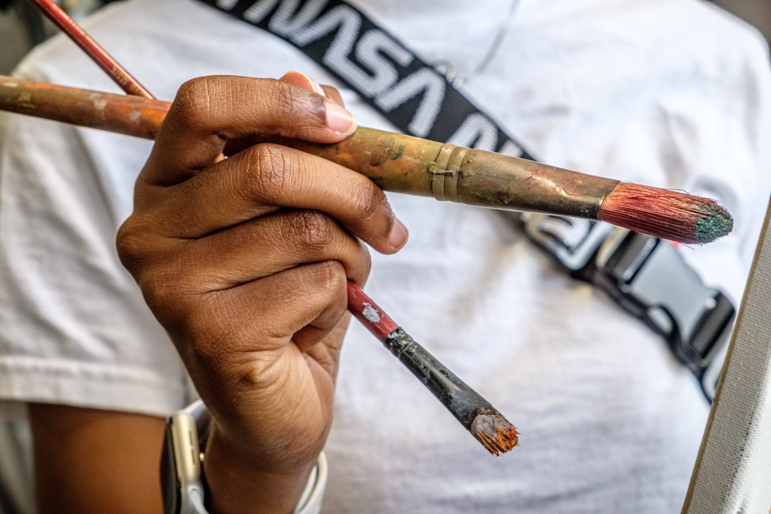 A close-up of a person holding two paint brushes