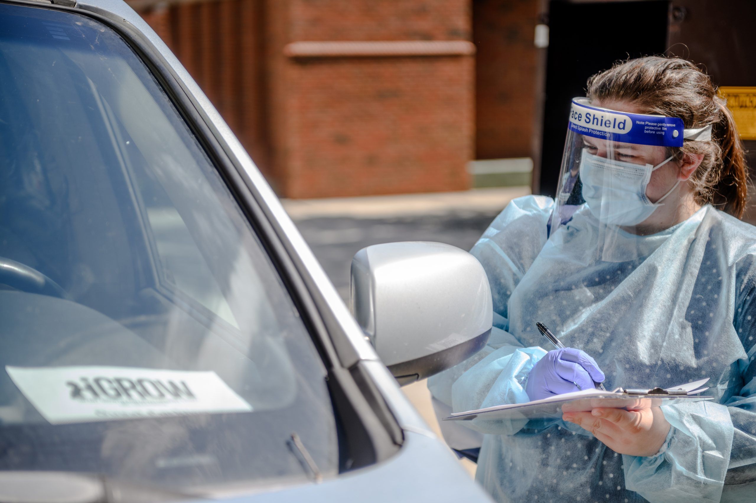 A researcher gathering data from a family by their car in July 2020 wearing a mask