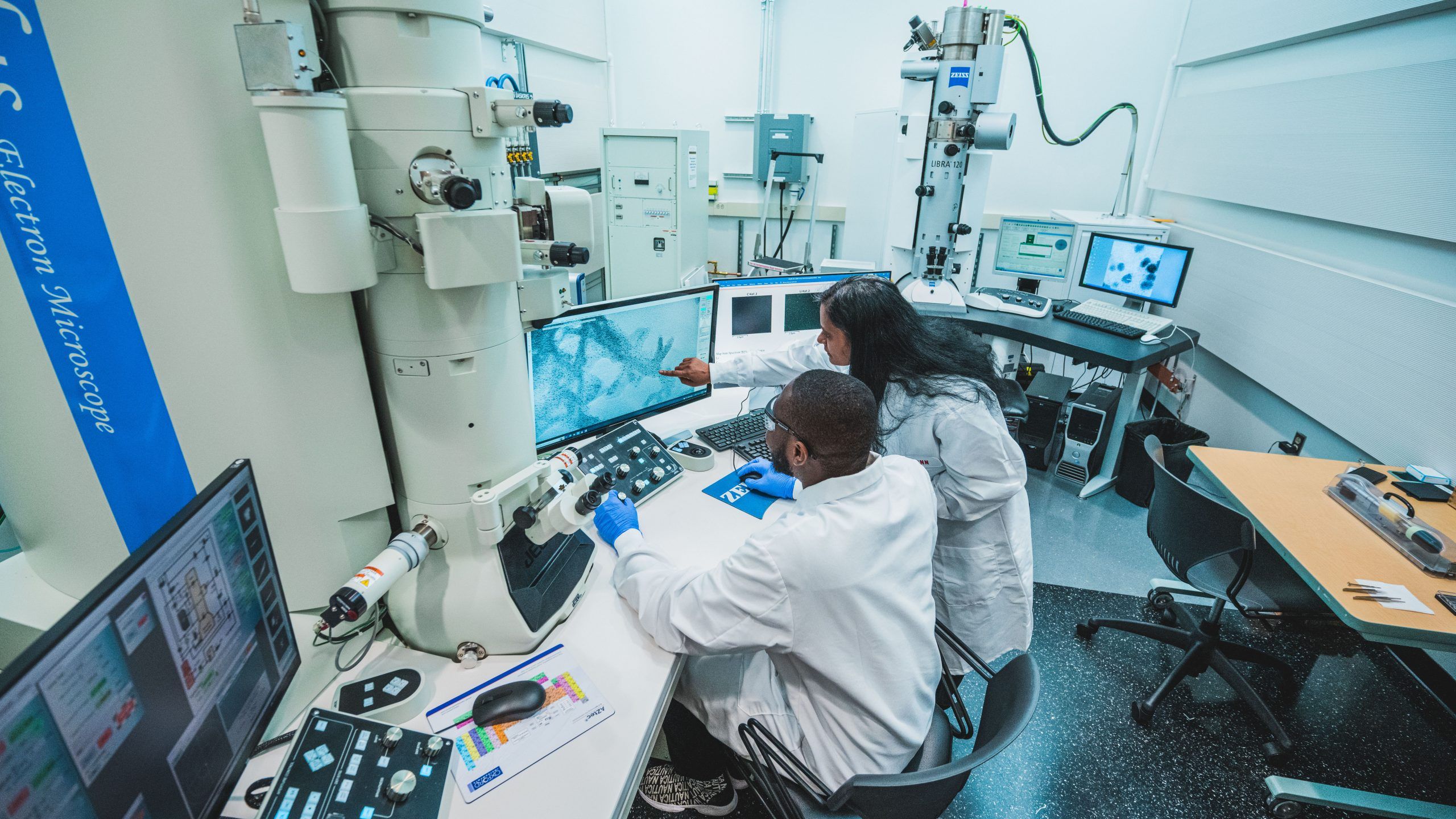 Two people in lab coats examining a computer monitor in a lab. 