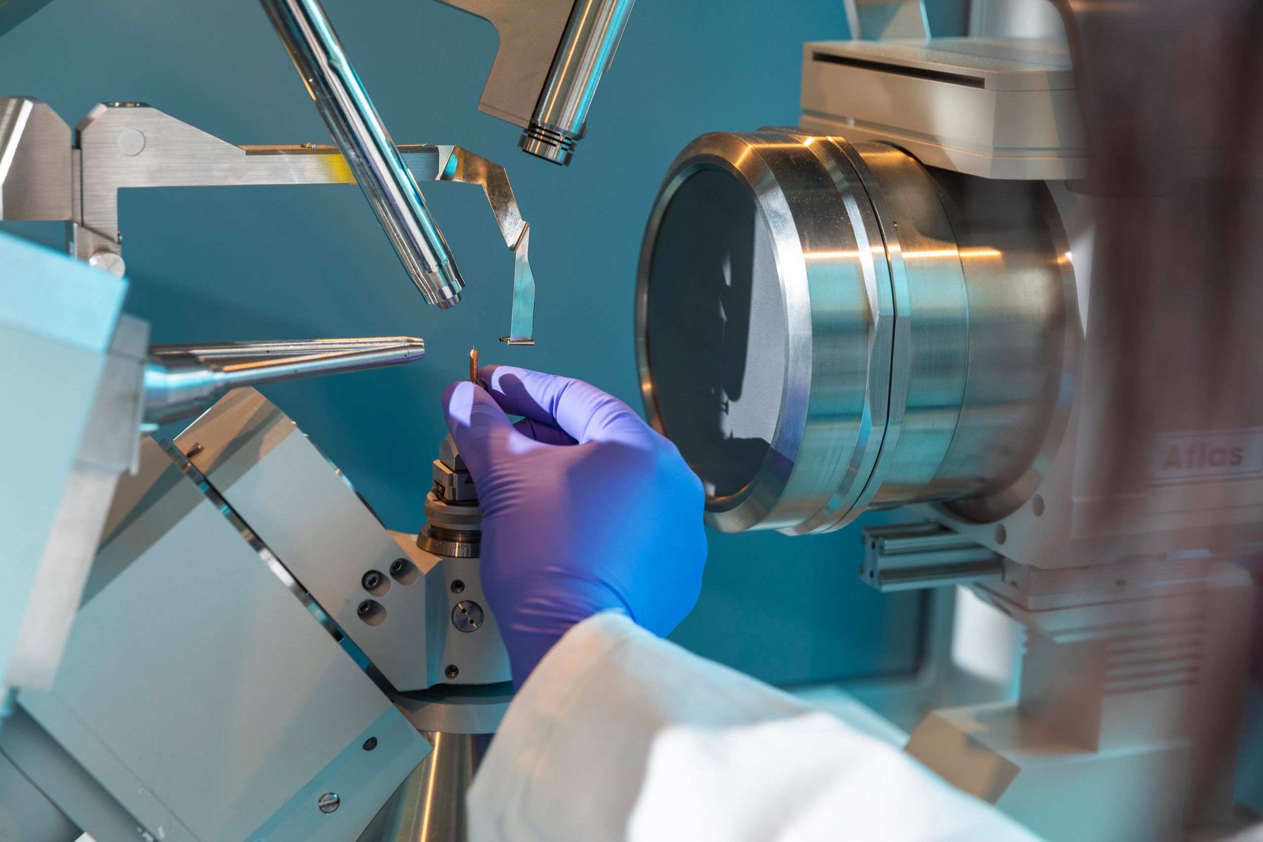 A close up of a hand in a protective glove placing an object into an x-ray crystallographer. 