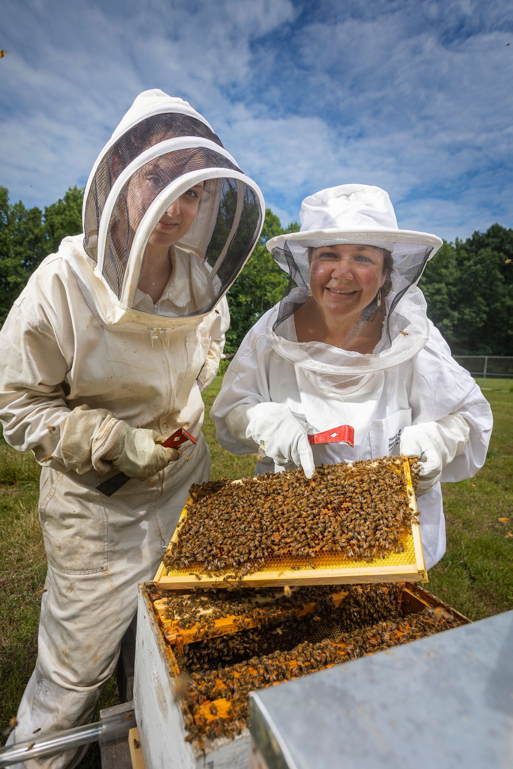 Synder and Wagoner wearing bee suits and pointing at a hive