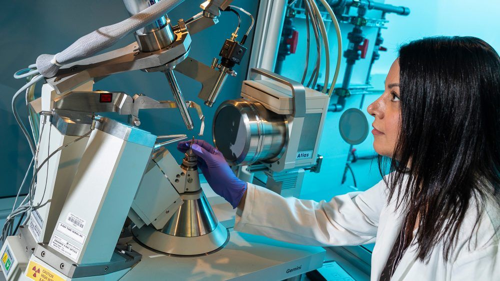 Dr. Hematian, wearing purple protective gloves and a lab coat adjusts a machine