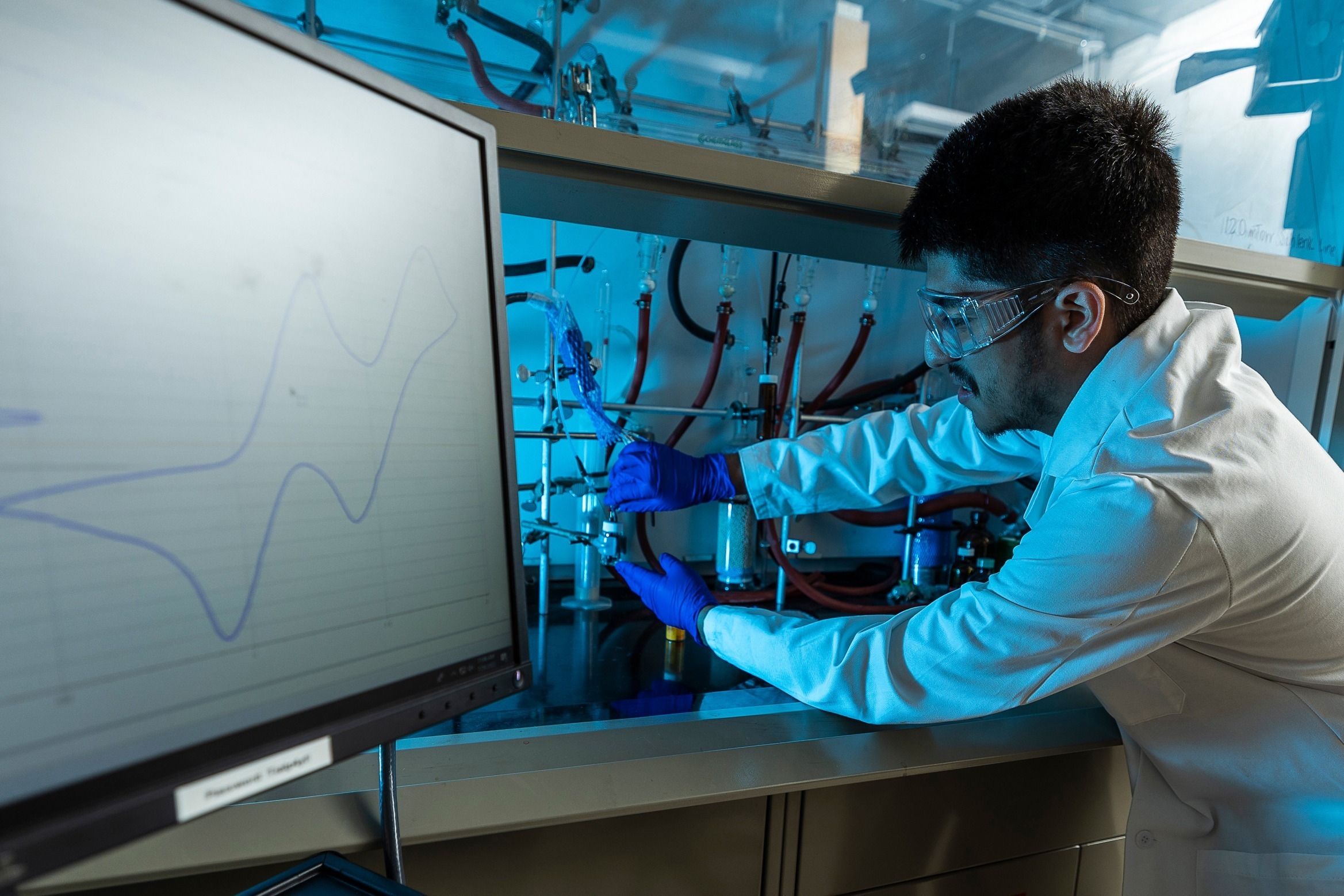 A person wearing a lab coat adjusts a valve in a lab