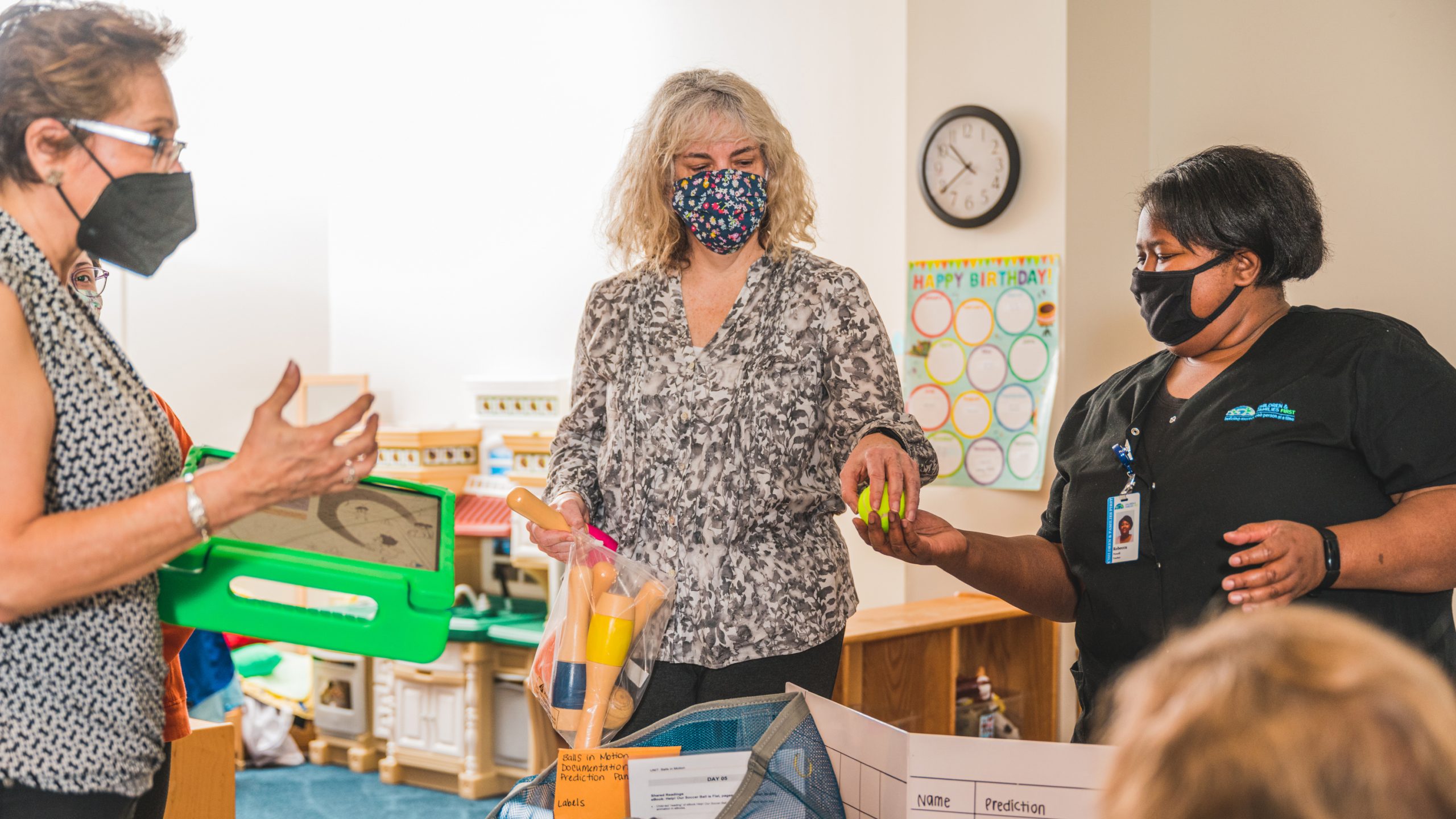 a person wearing a face mask and holding bowling pins and handing a ball to another person wearing a face mask