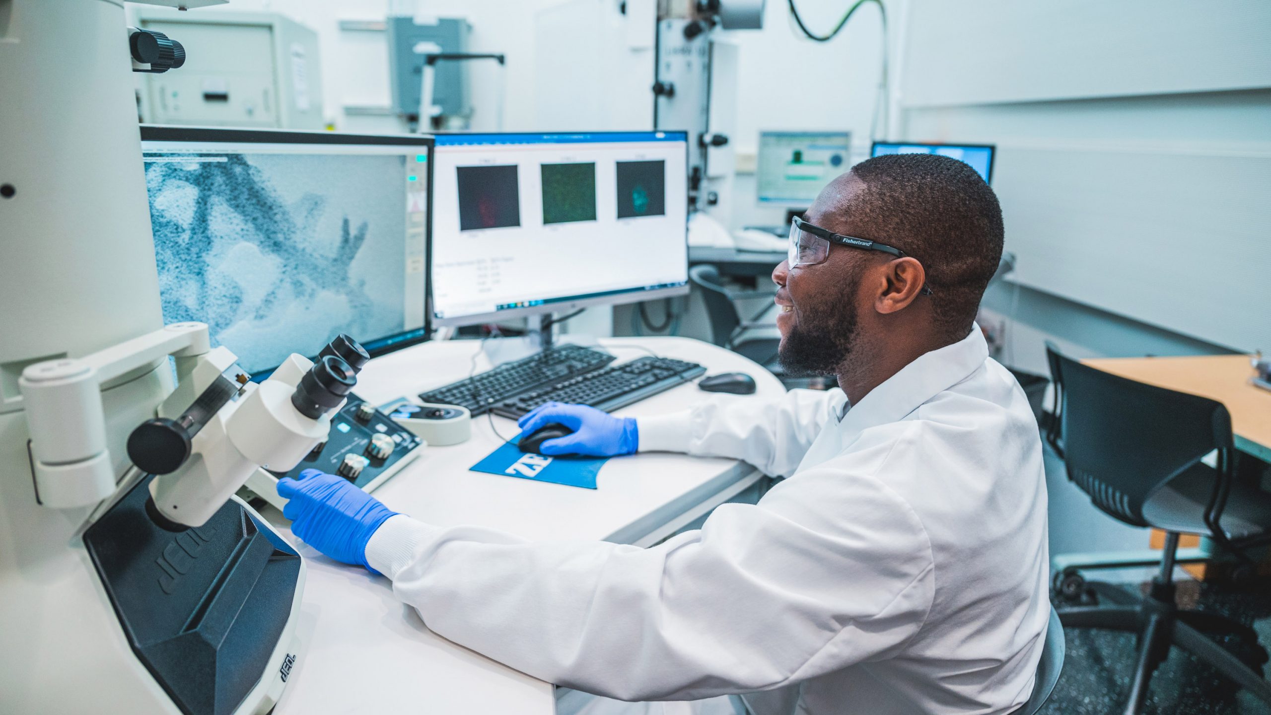 a person in a lab coat and gloves looking at a computer monitor