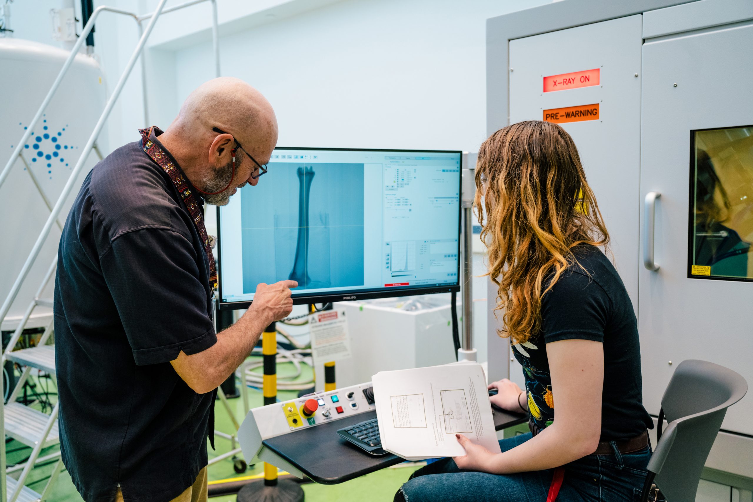 two people in a lab look at a computer monitor