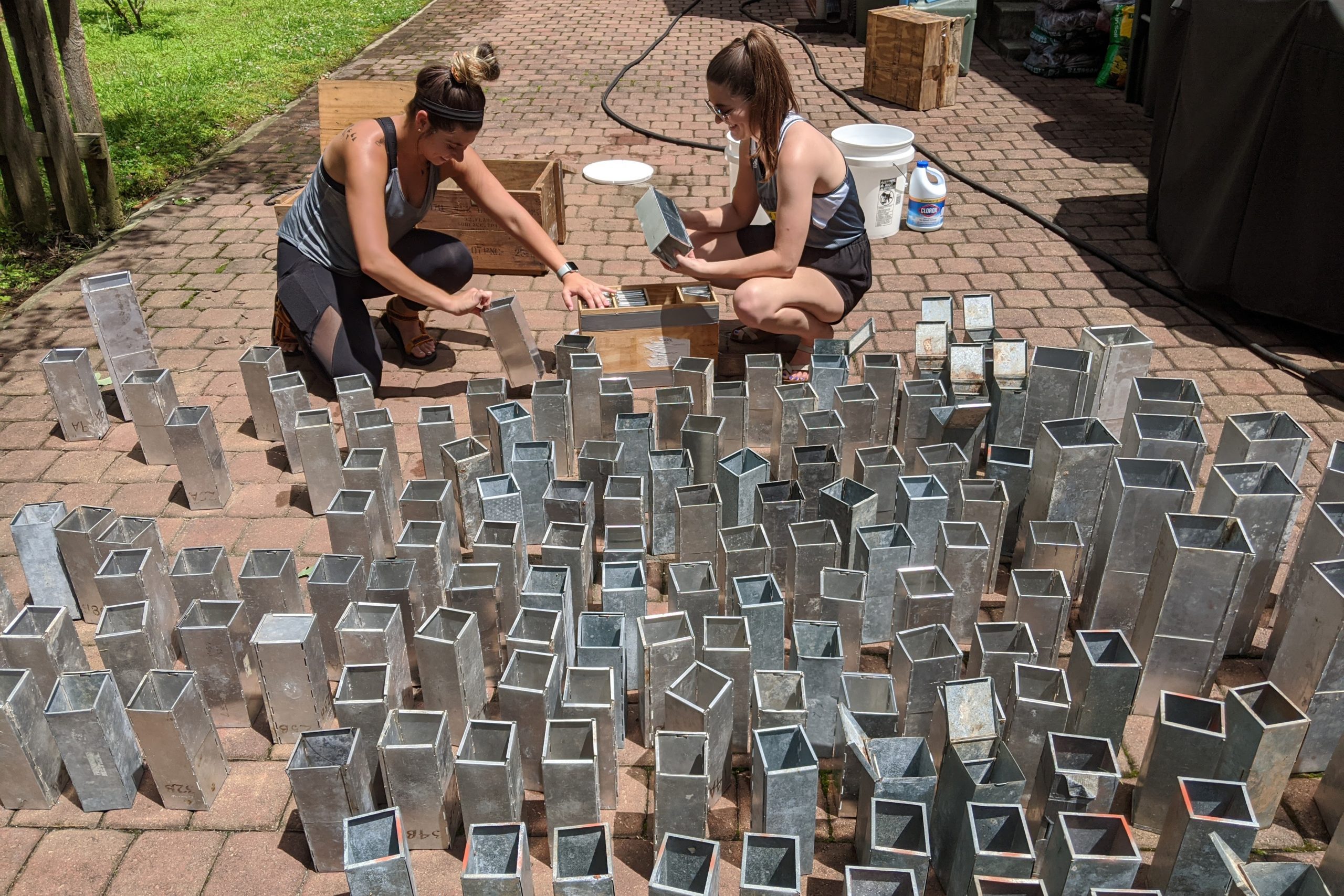 two women kneeling on a brick path with metal rectangular objects