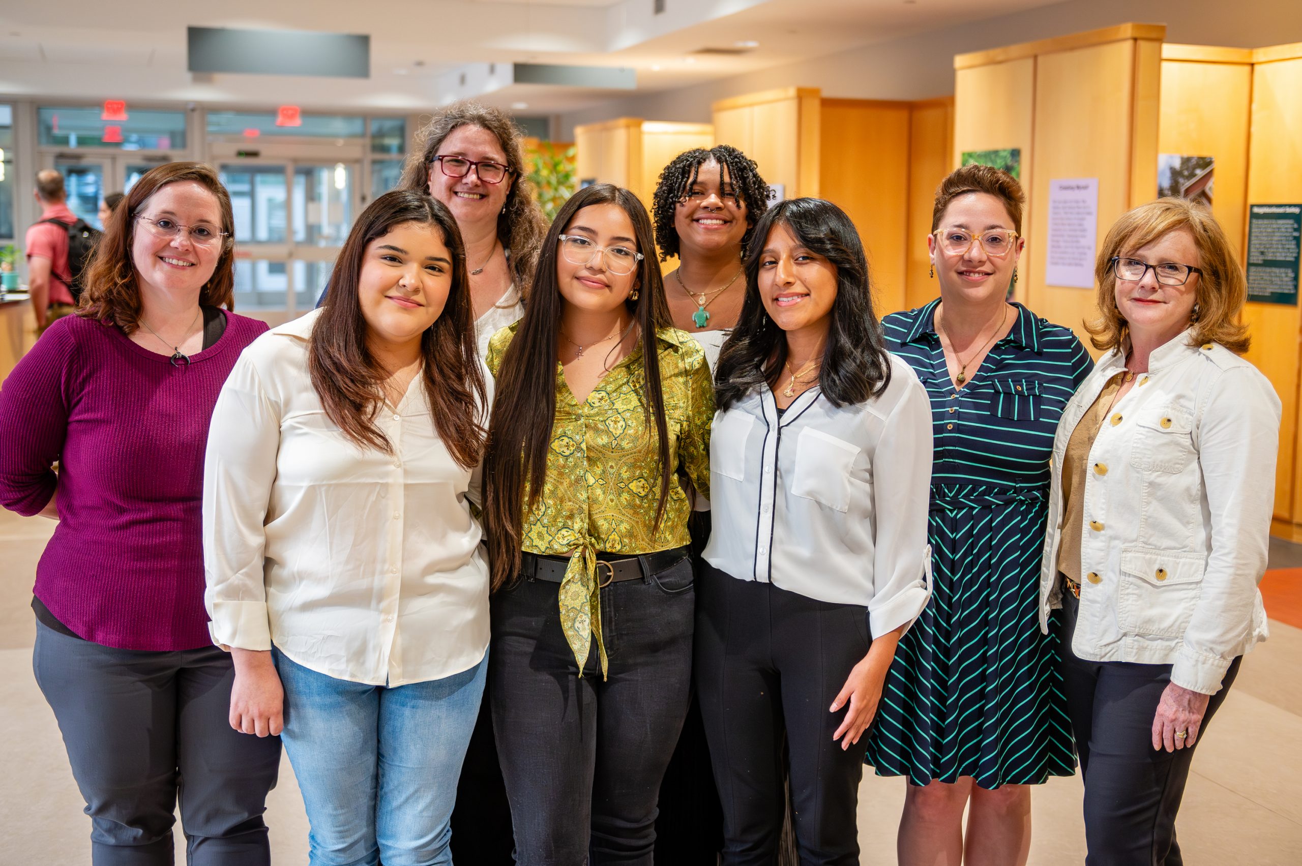 Members of the NC Health Transition team standing together in a brightly lit indoor space with wood-paneled walls and informational posters. The background includes glass doors leading outside and a person walking in the distance.
